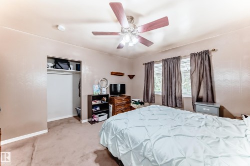Carpeted room featuring a ceiling fan with integrated lighting, three windows with blinds and curtain rods, and an open closet with a built-in shelf and hanging rod - 4006 115 Avenue, Edmonton, AB 