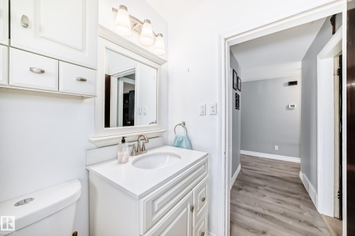Bathroom vanity featuring a white countertop with an undermount sink, brushed nickel faucet, and a framed mirror - 4006 115 Avenue, Edmonton, AB 