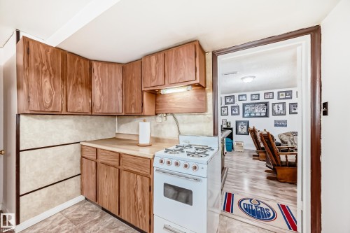 Compact kitchen featuring wood-finish cabinetry, a light-toned countertop, and a white freestanding range - 4006 115 Avenue, Edmonton, AB 