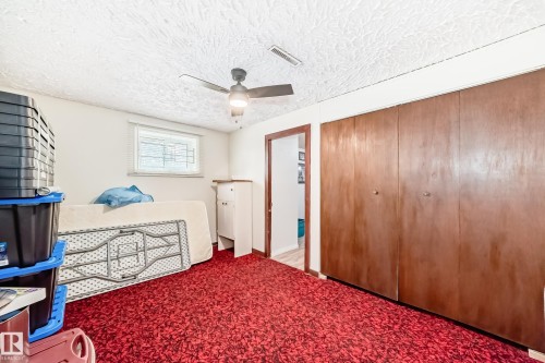 Room featuring wood-paneled bi-fold closet doors, a ceiling fan with integrated lighting, textured white ceiling, and a window with horizontal blinds - 4006 115 Avenue, Edmonton, AB 