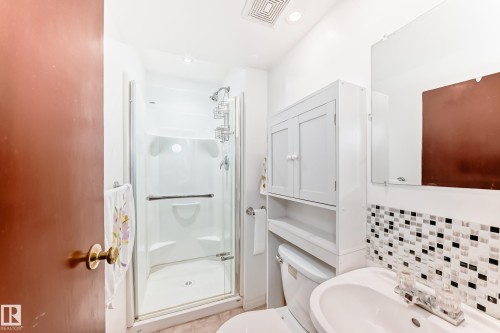 Bathroom featuring a glass-enclosed shower, white vanity with integrated sink, chrome faucet, and a mosaic tile backsplash - 4006 115 Avenue, Edmonton, AB 
