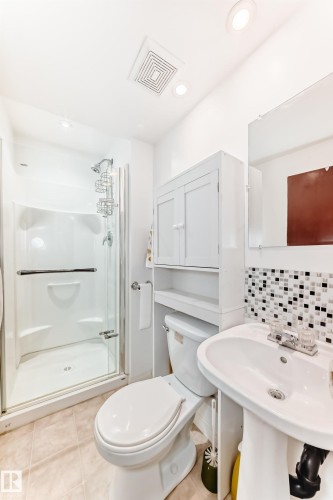 Bathroom featuring a glass-enclosed shower with a white acrylic surround, a pedestal sink, a toilet, and a white storage cabinet - 4006 115 Avenue, Edmonton, AB 