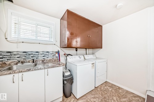 Dedicated utility space featuring a built-in sink, white cabinetry, and a mosaic tile backsplash - 4006 115 Avenue, Edmonton, AB 