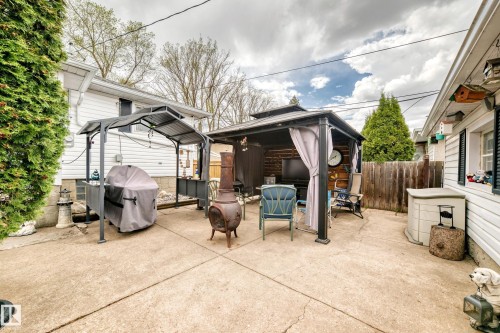 Expansive concrete patio area featuring a privacy fence, mature perimeter trees, and permanent metal gazebo structures - 4006 115 Avenue, Edmonton, AB 