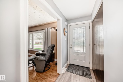 Entryway with light wood-finish flooring, white paneled entry door with decorative glass inserts, and a dark wood bifold closet door - 4006 115 Avenue, Edmonton, AB 