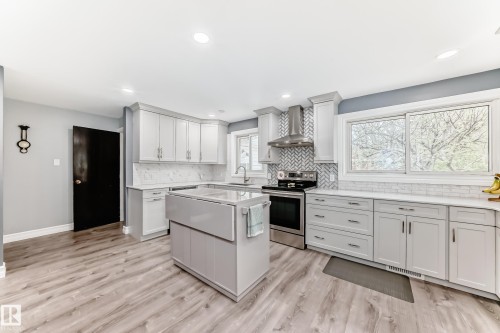 Modern kitchen featuring light gray cabinetry, white countertops, stainless steel appliances, herringbone tile backsplash, and light wood-finish flooring - 4006 115 Avenue, Edmonton, AB 