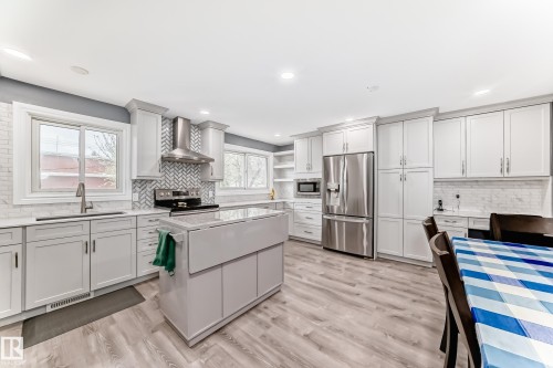 Modern kitchen featuring light gray cabinetry, stainless steel appliances, a center island, wood-finish flooring, and recessed lighting - 4006 115 Avenue, Edmonton, AB 