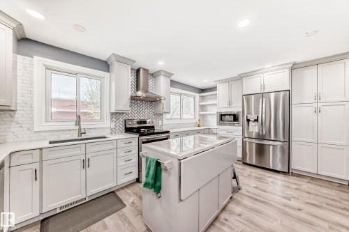 Modern kitchen featuring light cabinetry, stainless steel appliances, a center island with a built-in extension, white countertops, and wood-finish flooring - 4006 115 Avenue, Edmonton, AB 