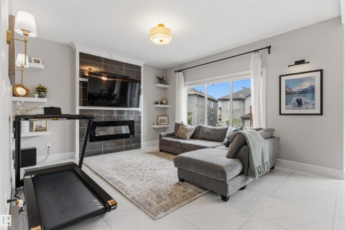 Spacious living area featuring a built-in fireplace with dark tile surround, a large window, white tile flooring, and recessed lighting - 3312 11 Avenue, Edmonton, AB - Indoor Photo Showing Living Room With Fireplace