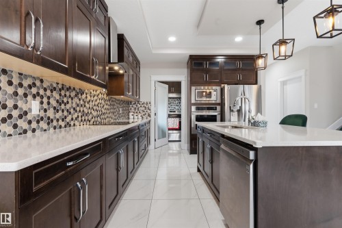 Spacious kitchen featuring dark wood cabinetry, light-toned countertops, and a full-height hexagonal tile backsplash - 3312 11 Avenue, Edmonton, AB - Indoor Photo Showing Kitchen With Upgraded Kitchen