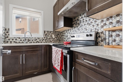 Kitchen area featuring dark wood-finish cabinetry, light-toned countertops, a stainless steel faucet, and a hexagonal tile backsplash - 3312 11 Avenue, Edmonton, AB - Indoor Photo Showing Kitchen