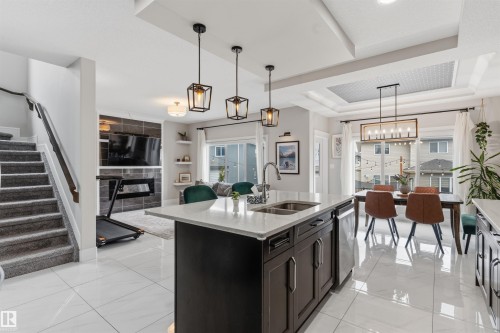 Open-concept interior featuring a kitchen island with dual sinks, white tile flooring, and a dining area with a coffered ceiling - 3312 11 Avenue, Edmonton, AB - Indoor Photo Showing Kitchen With Double Sink With Upgraded Kitchen