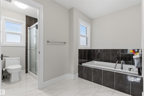 Modern bathroom featuring an integrated soaking tub with dark stone-finish surround, a separate glass-enclosed shower, and a white toilet - 3312 11 Avenue, Edmonton, AB - Indoor Photo Showing Bathroom