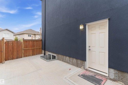Exterior access featuring a paneled door, wall-mounted light fixture, concrete patio, and a wood fence - 3312 11 Avenue, Edmonton, AB - Outdoor With Exterior