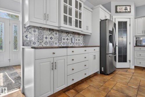 White shaker-style cabinetry with varied storage options, a patterned tile backsplash, and a stainless steel refrigerator - 34 Valleyview Ridge, Fort Saskatchewan, AB - Indoor Photo Showing Kitchen