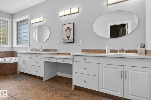 Dual vanity with white cabinetry and built-in makeup counter, featuring a corner soaking tub and glass block windows - 34 Valleyview Ridge, Fort Saskatchewan, AB - Indoor Photo Showing Bathroom