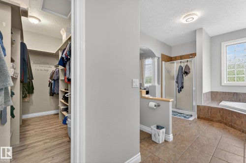 Integrated bathroom and walk-in closet featuring a tiled shower enclosure, a built-in soaking tub with tiled surround, and a walk-in closet with wood-finish flooring and built-in shelving - 34 Valleyview Ridge, Fort Saskatchewan, AB - Indoor