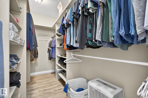 Walk-in closet featuring wood-finish flooring, built-in shelving, multiple hanging rods, and a ceiling-mounted light fixture - 34 Valleyview Ridge, Fort Saskatchewan, AB - Indoor With Storage