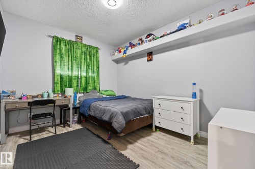Bedroom featuring wood-finish flooring, light gray walls, a window with green drapery, and a white floating shelf - 34 Valleyview Ridge, Fort Saskatchewan, AB - Indoor Photo Showing Bedroom
