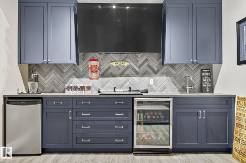 Custom wet bar featuring a herringbone tile backsplash, two-tone cabinetry, and wood-finish flooring - 34 Valleyview Ridge, Fort Saskatchewan, AB - Indoor Photo Showing Kitchen