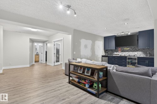 Entertainment space featuring wood-finish flooring, recessed lighting, and a built-in wet bar with dark blue cabinetry, a beverage refrigerator, and a herringbone tile backsplash - 34 Valleyview Ridge, Fort Saskatchewan, AB - Indoor