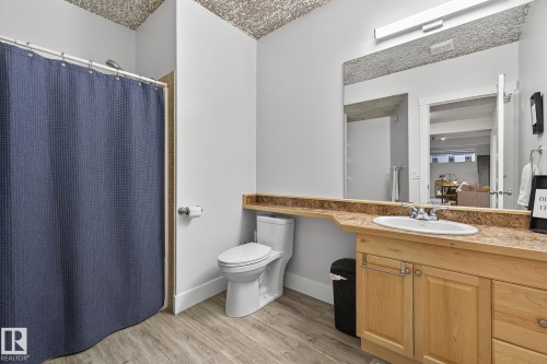 Bathroom featuring wood-finish flooring, a light wood vanity with cabinet storage and drawers, a rectangular undermount sink, and a large wall-mounted mirror with overhead lighting - 34 Valleyview Ridge, Fort Saskatchewan, AB - Indoor Photo Showing Bathroom