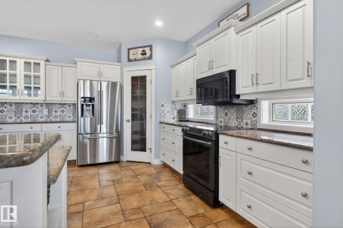 Kitchen featuring white cabinetry, granite countertops, patterned tile backsplash, stainless steel refrigerator, and ceramic tile flooring - 34 Valleyview Ridge, Fort Saskatchewan, AB - Indoor Photo Showing Kitchen