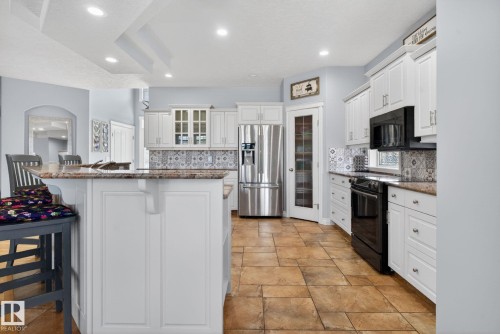 Kitchen featuring white cabinetry, stainless steel refrigerator, black range, patterned tile backsplash, and a breakfast bar with stone-finish countertop - 34 Valleyview Ridge, Fort Saskatchewan, AB - Indoor Photo Showing Kitchen With Upgraded Kitchen
