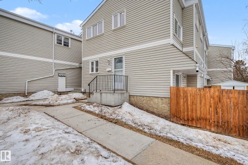 The property features light-colored horizontal siding, a concrete walkway, and a wooden privacy fence - 6F Castle Terrace, Edmonton, AB - Outdoor