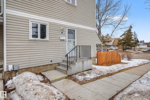 The property features a light-colored siding exterior, an entrance with concrete steps and a metal handrail, and a small fenced area - 6F Castle Terrace, Edmonton, AB - Outdoor