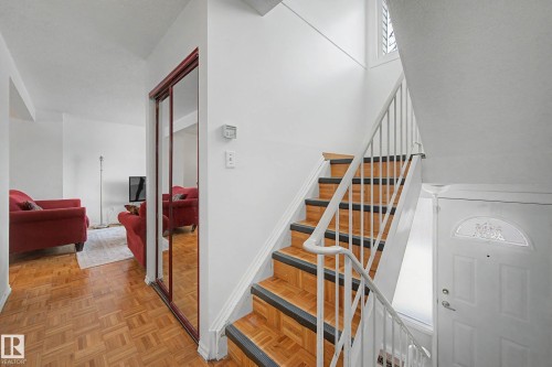 The property features parquet flooring, a staircase with white railings, and a mirrored closet - 6F Castle Terrace, Edmonton, AB - Indoor Photo Showing Other Room