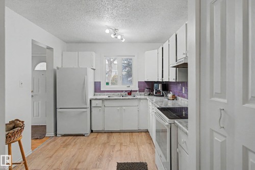 The kitchen features wood-look flooring, white cabinetry, a purple tile backsplash, and a window providing natural light - 6F Castle Terrace, Edmonton, AB - Indoor Photo Showing Kitchen