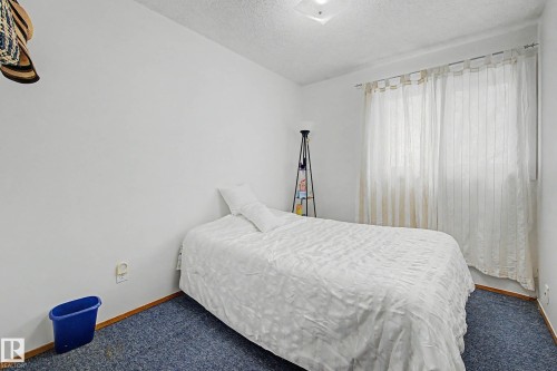 The room features a neutral color palette with white walls, blue carpeting, and a window with white curtains - 6F Castle Terrace, Edmonton, AB - Indoor Photo Showing Bedroom