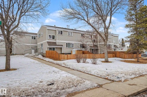 The property features a multi-story exterior with light-colored siding, a wooden fence, and mature trees on the surrounding grounds - 6F Castle Terrace, Edmonton, AB - Outdoor