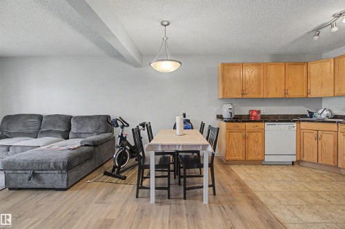 Open-concept living space featuring a kitchen with wood cabinetry and dark countertops, a white dishwasher, and track lighting - 204 309 Clareview Station Drive, Edmonton, AB - Indoor