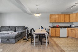 Open-concept living space featuring a kitchen with wood cabinetry and dark countertops, a white dishwasher, and track lighting - 