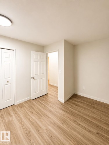 Wood-finish flooring, white paneled doors, and a flush-mount ceiling light fixture - 13833 24 Street Nw, Edmonton, AB - Indoor Photo Showing Other Room