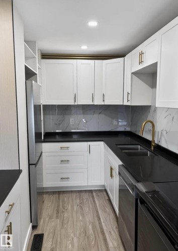 Kitchen featuring white shaker-style cabinetry, dark countertops, a light-toned wood-finish floor, and a patterned backsplash - 13833 24 Street W, Edmonton, AB - Indoor Photo Showing Kitchen With Double Sink