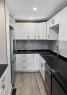 Kitchen featuring white shaker-style cabinetry, dark countertops, a light-toned wood-finish floor, and a patterned backsplash - 13833 24 Street W, Edmonton, AB  - Indoor Photo Showing Kitchen With Double Sink 