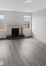 Living area featuring a white-painted brick fireplace with a dark hearth, wood-finish flooring, two large windows, and a flush-mount ceiling light - 13833 24 Street W, Edmonton, AB  - Indoor Photo Showing Living Room With Fireplace 