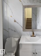 Bathroom featuring white and gold veined wall panels, a white vanity with shaker-style cabinetry, an integrated white sink, and a gold-finish faucet - 