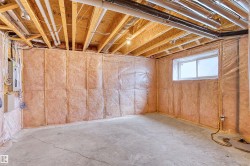 Unfinished basement space featuring exposed wood joists, insulated exterior walls, a concrete floor, and an egress window - 