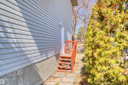 Exterior side entrance featuring light-toned horizontal siding and a red-stained wooden staircase - 15504 102 Avenue Nw, Edmonton, AB - Outdoor