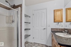 Glass-enclosed shower with tiled surround, wood-finish vanity with integrated sink, full-width mirror, built-in shelving, and paneled door - 