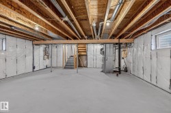 Expansive open lower level featuring a concrete floor, exposed wood ceiling joists, and visible utility systems - 