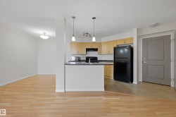 Open-concept kitchen featuring light wood-finish cabinetry, dark countertops, black appliances, and a breakfast bar with pendant lighting - 