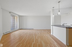 Open-concept living area featuring wood-finish flooring, a sliding glass door, and white baseboard heating - 