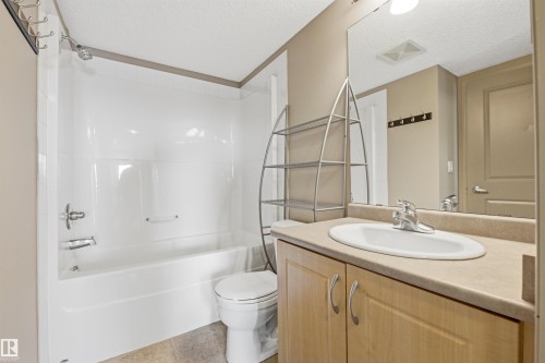 Bathroom featuring a complete tub and shower unit, a light wood-finish vanity with a single sink, an integrated countertop, and a large wall-mounted mirror - 407 11453 Ellerslie Road Sw, Edmonton, AB - Indoor Photo Showing Bathroom