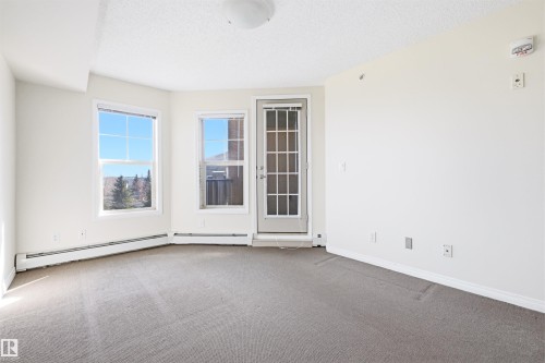 Bright interior room featuring neutral-toned carpet, white painted walls, and a textured ceiling - 407 11453 Ellerslie Road Sw, Edmonton, AB - Indoor Photo Showing Other Room