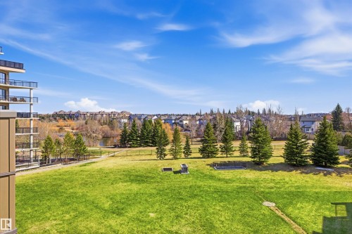 Expansive green space featuring mature evergreen trees and a water feature in the background - 407 11453 Ellerslie Road Sw, Edmonton, AB - Outdoor With View